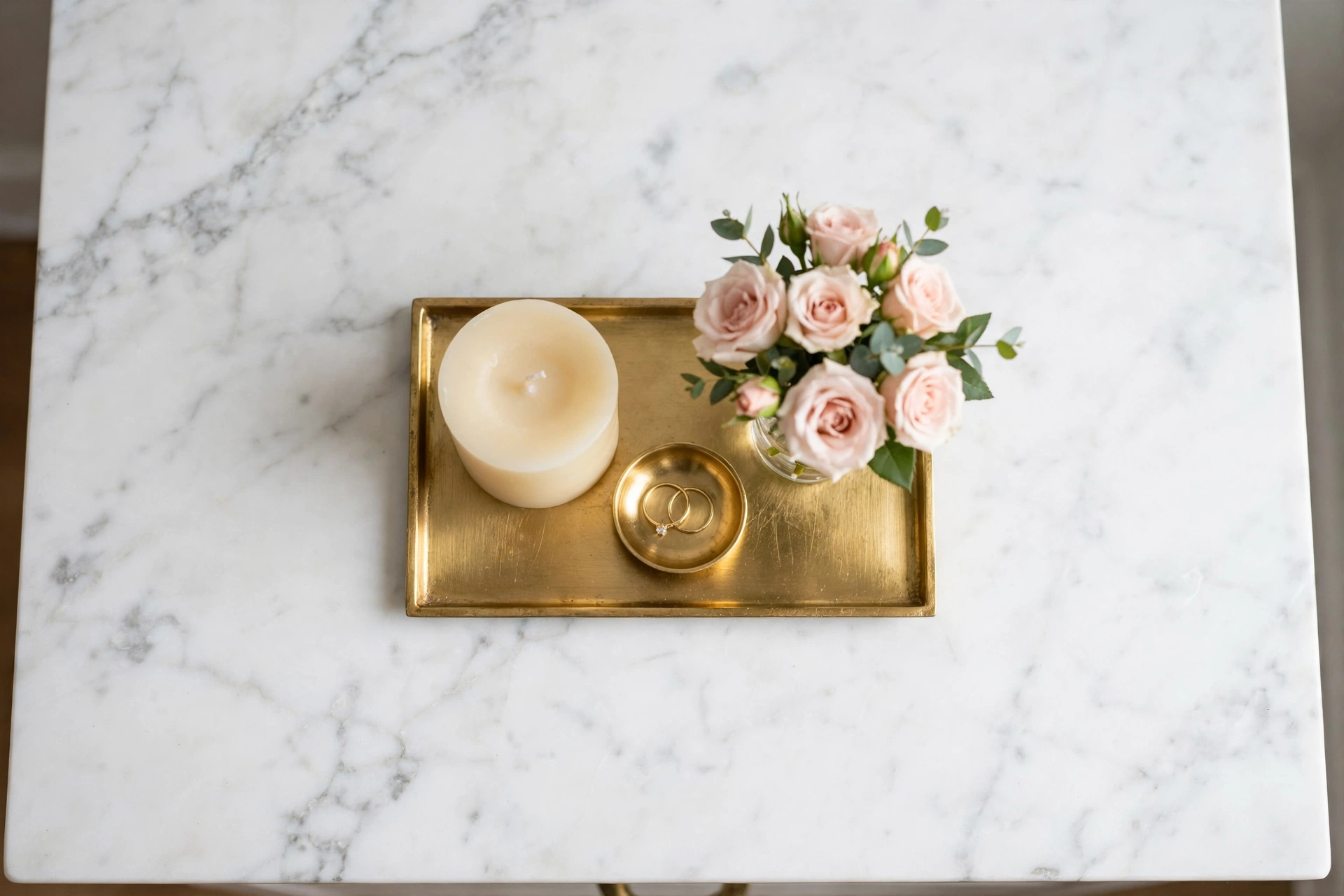 Small gold tray on a nightstand holding a candle, a ring dish, and a small vase seen from above